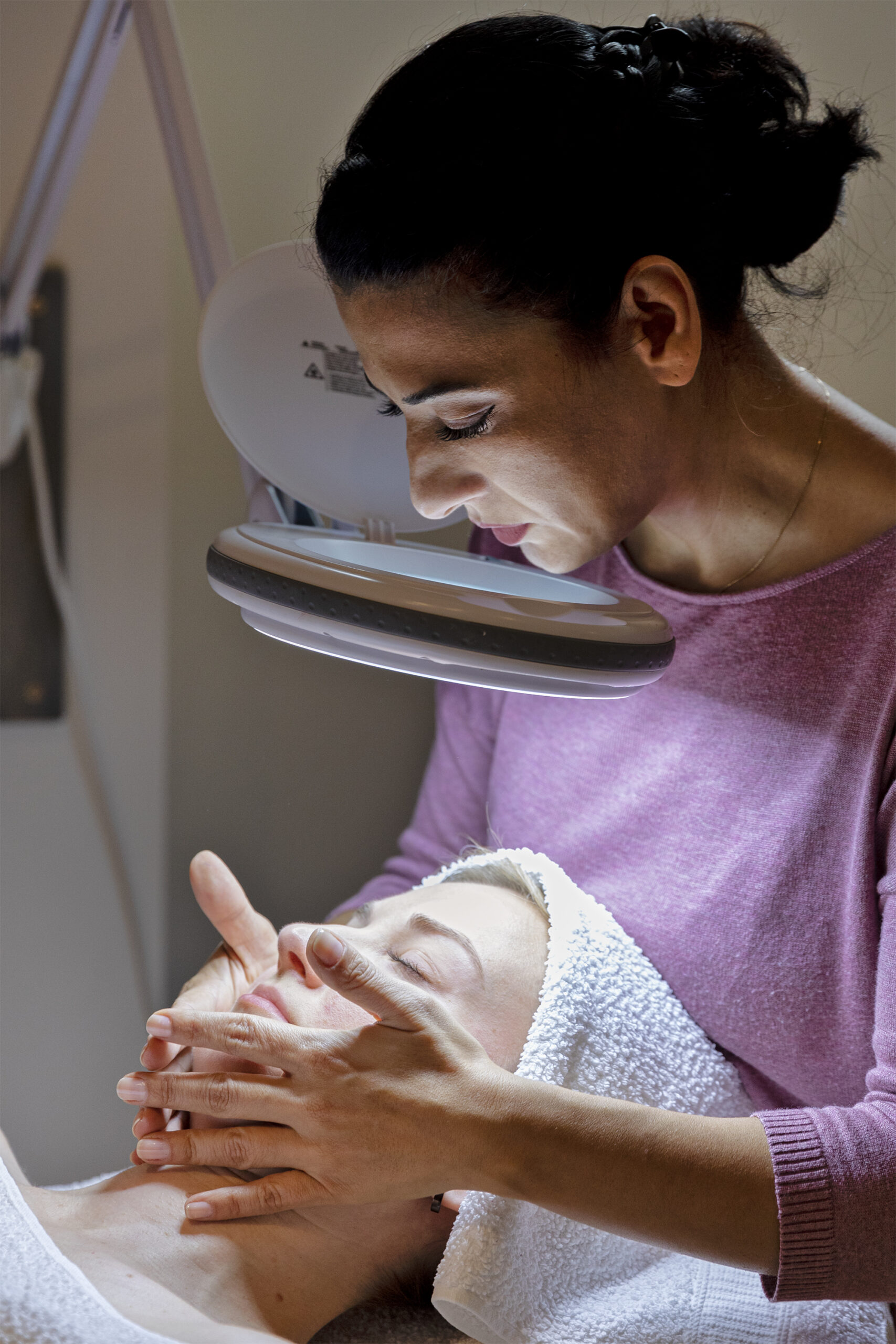 Kosmetikerin führt professionelle Gesichtsbehandlung unter Vergrößerungslampe durch